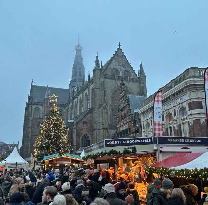 A crowded Christmas market in front of a cathedral on a foggy day.